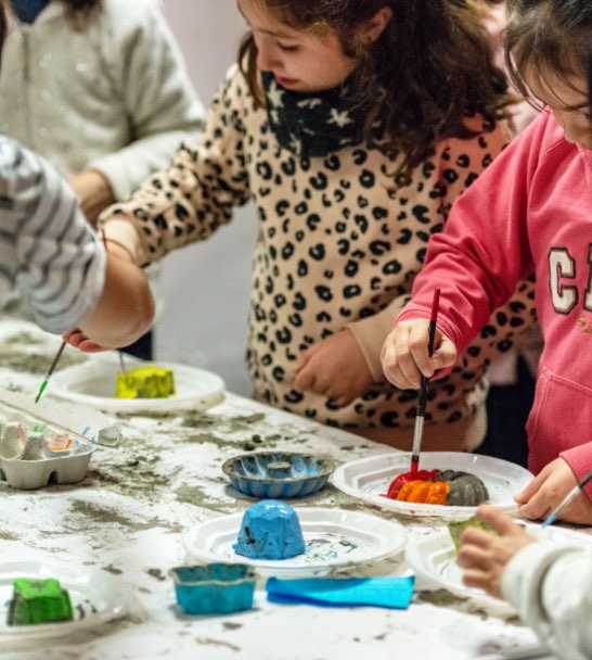niños alrededor de una mesa pintando esculturas de cemento.